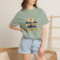 Woman wearing a bay t-shirt printed with the Faith Over Fear design, standing beside a wooden ladder and a woven basket against a plain wall