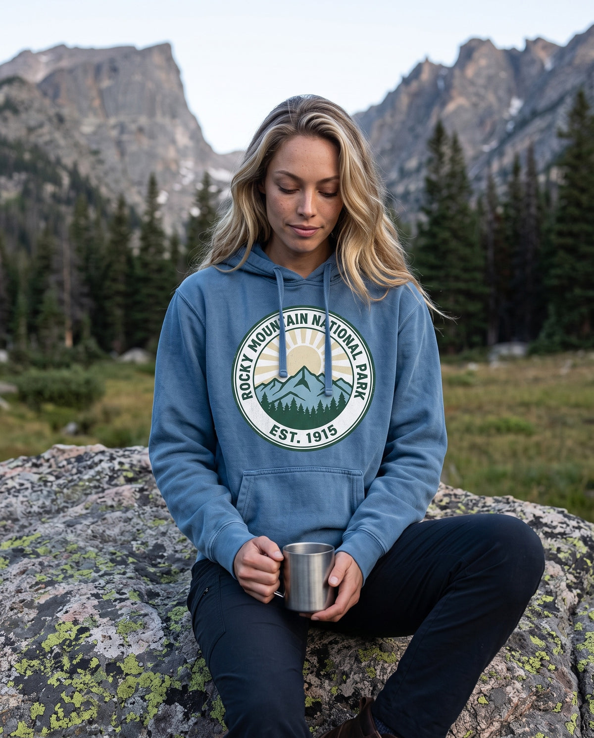 Rocky Mountain National Park EST 1915 hoodie worn on a granite boulder below the peaks with a steel mug