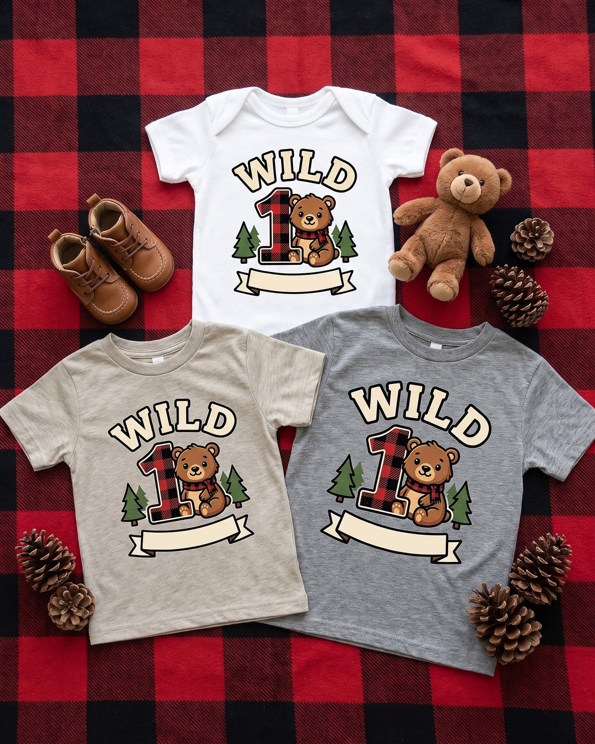 Flat lay of the Wild One plaid bear first birthday design across matching kids garments with playful props
