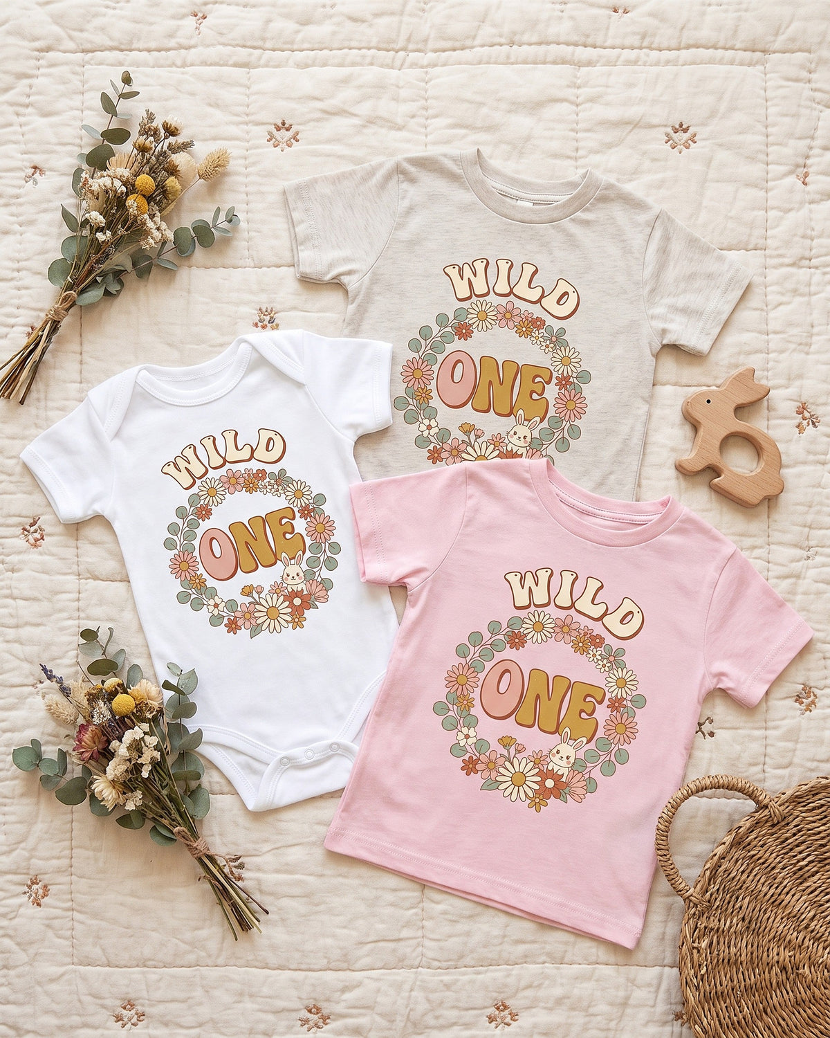 Flat lay of the Wild One boho floral bunny first birthday design across matching kids garments with playful props
