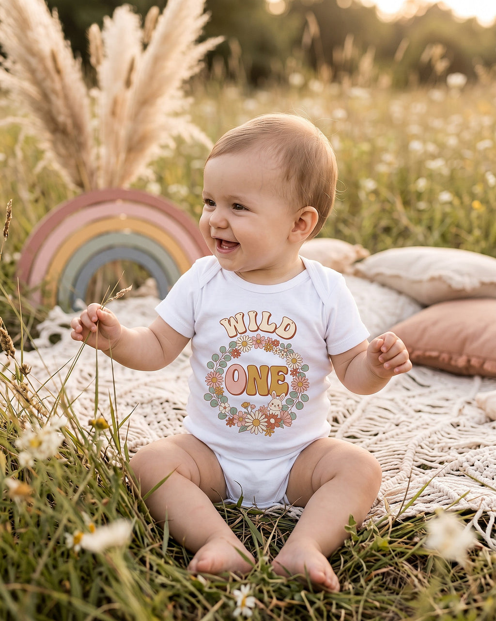 Wild One boho floral bunny first birthday design on a white baby bodysuit worn by a happy baby