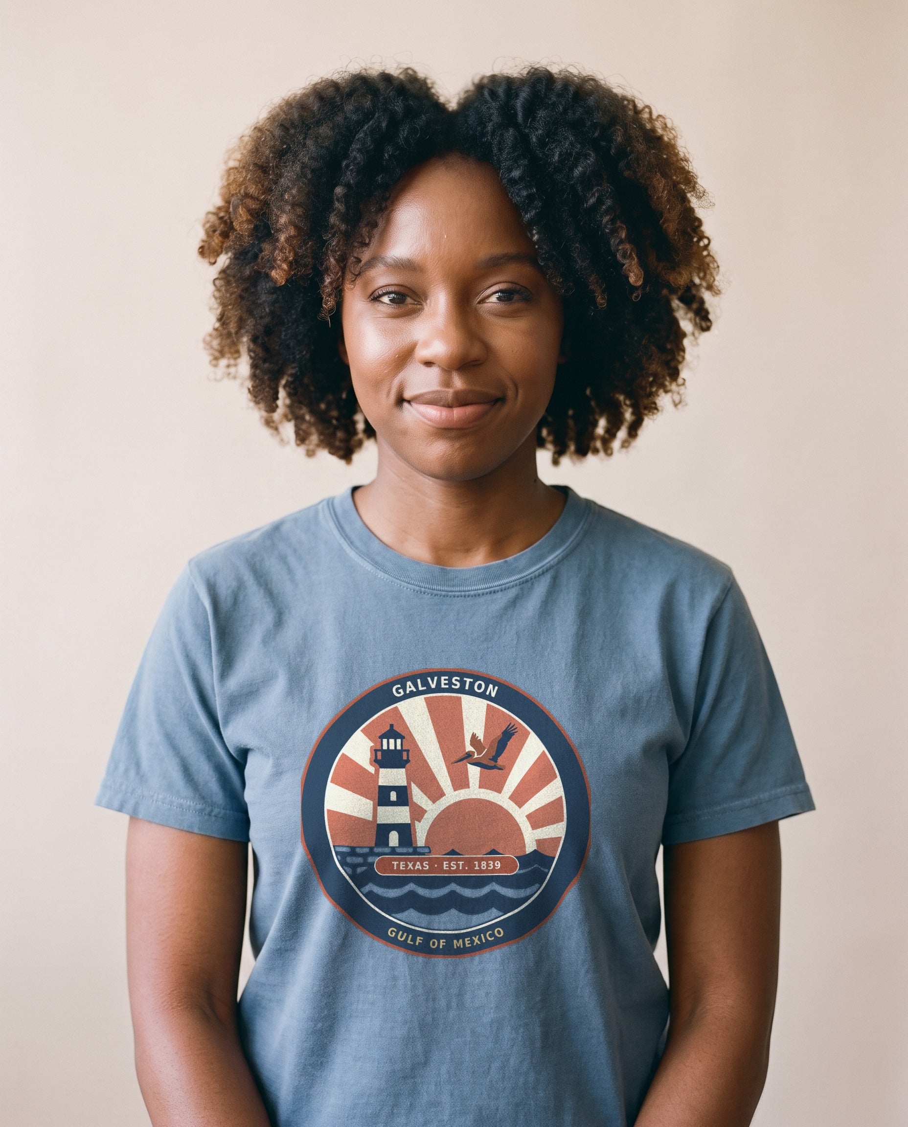 Woman wearing the Galveston Texas vintage coastal badge tee in Blue Jean, lighthouse and gulf sunset badge