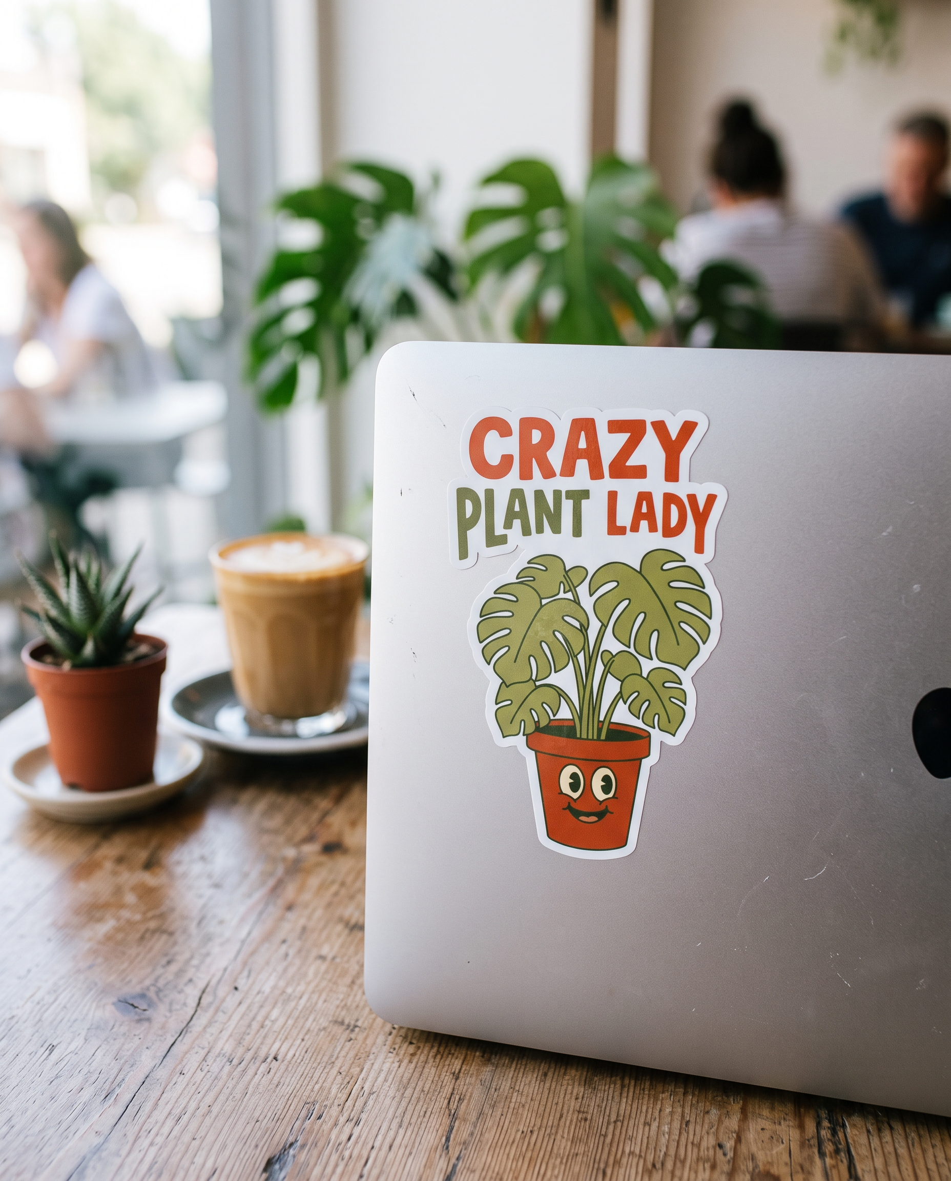 Crazy Plant Lady sticker on a laptop lid in a plant-filled cafe