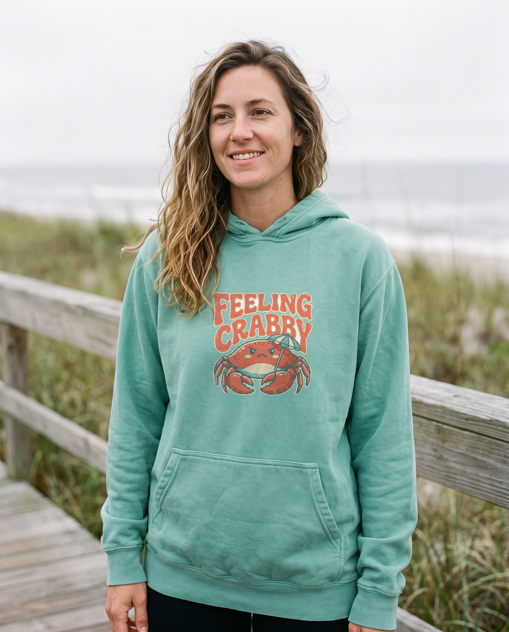 Feeling Crabby seafoam hoodie on model at a coastal boardwalk, print centered