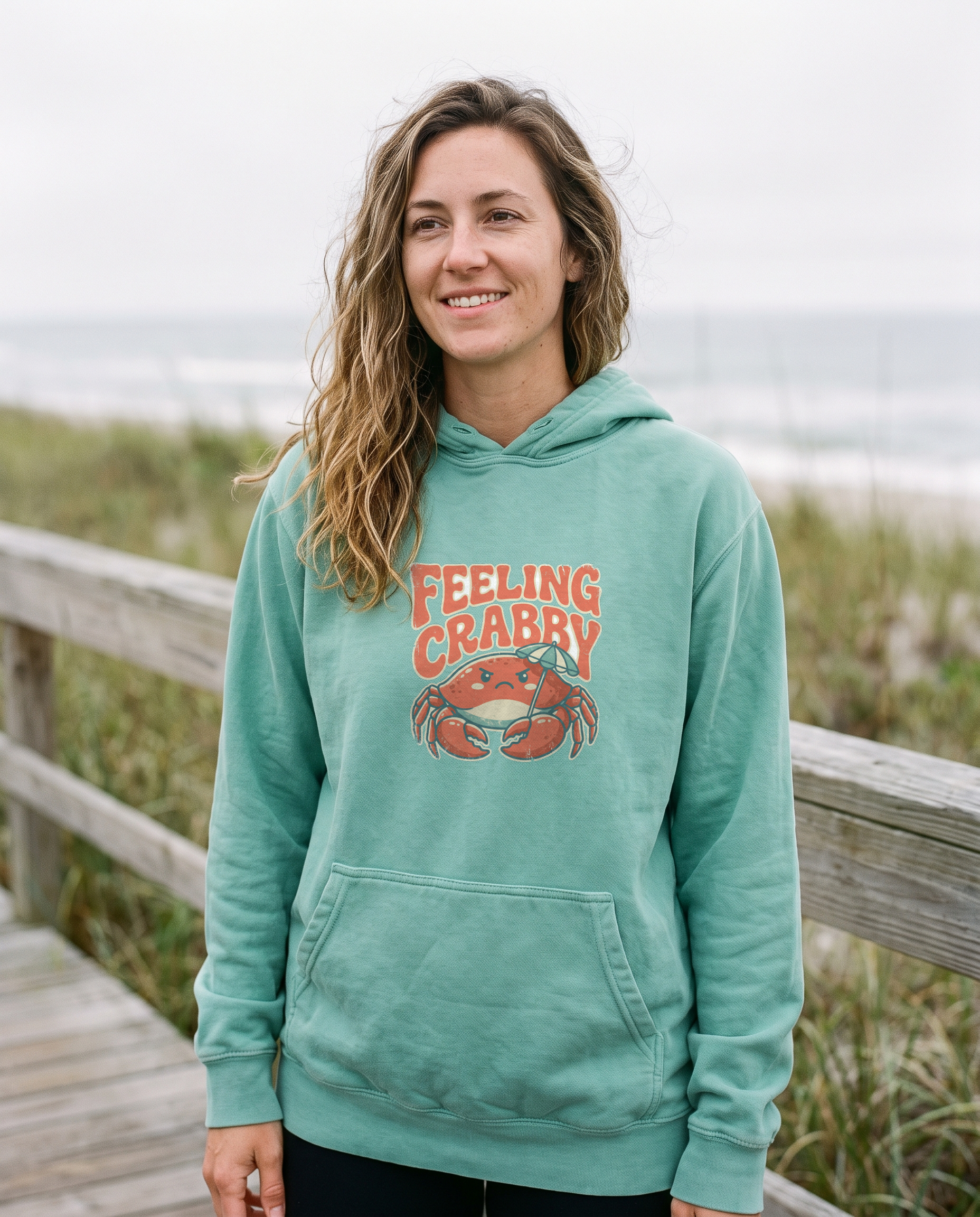 Feeling Crabby seafoam hoodie on model at a coastal boardwalk, print centered