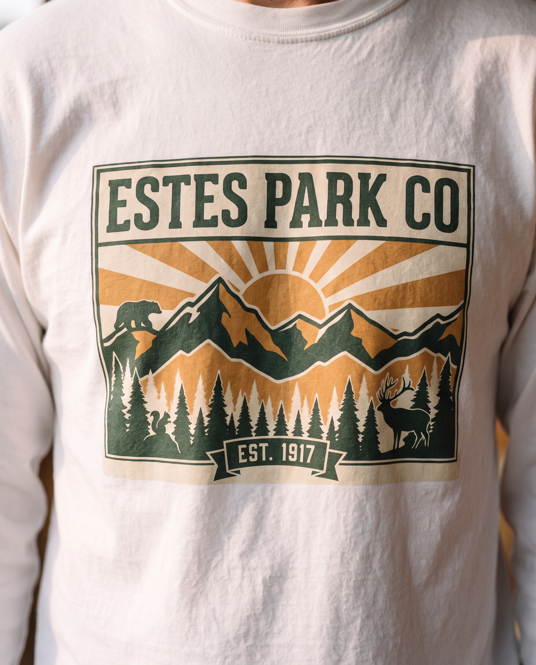 Estes Park CO hidden wildlife badge close-up on an ivory Comfort Colors long sleeve tee, bear elk and squirrel design, EST. 1917