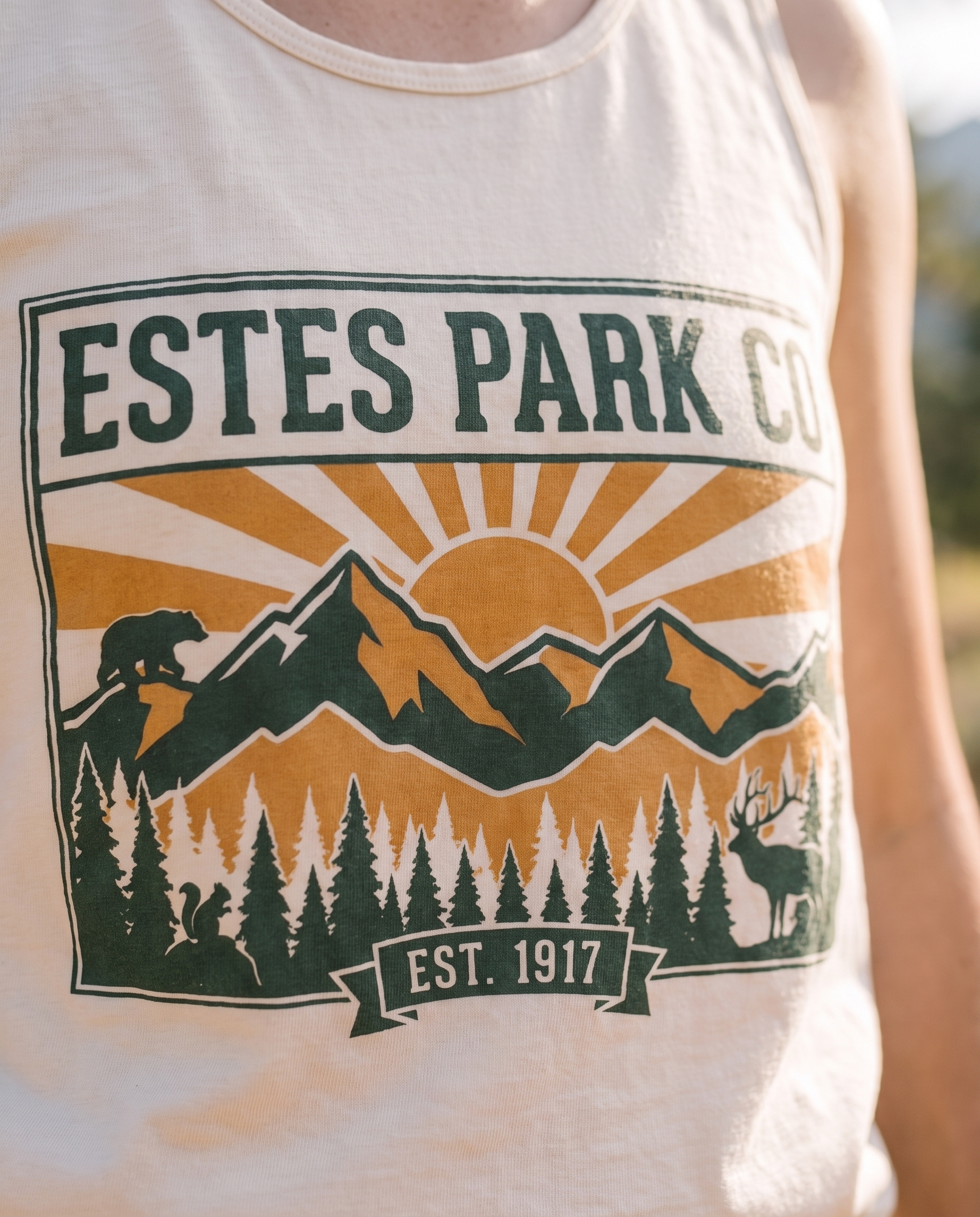 Estes Park CO hidden wildlife badge close-up on an ivory Comfort Colors tank top, bear elk and squirrel design, EST. 1917