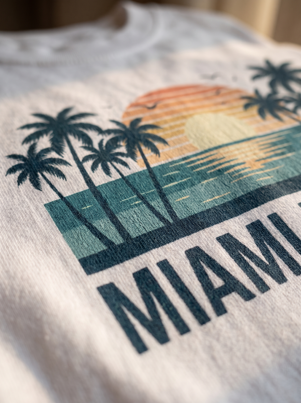 Close up of the Miami Beach retro screen print, teal sunset palms and MIAMI BEACH wordmark ink in the cotton