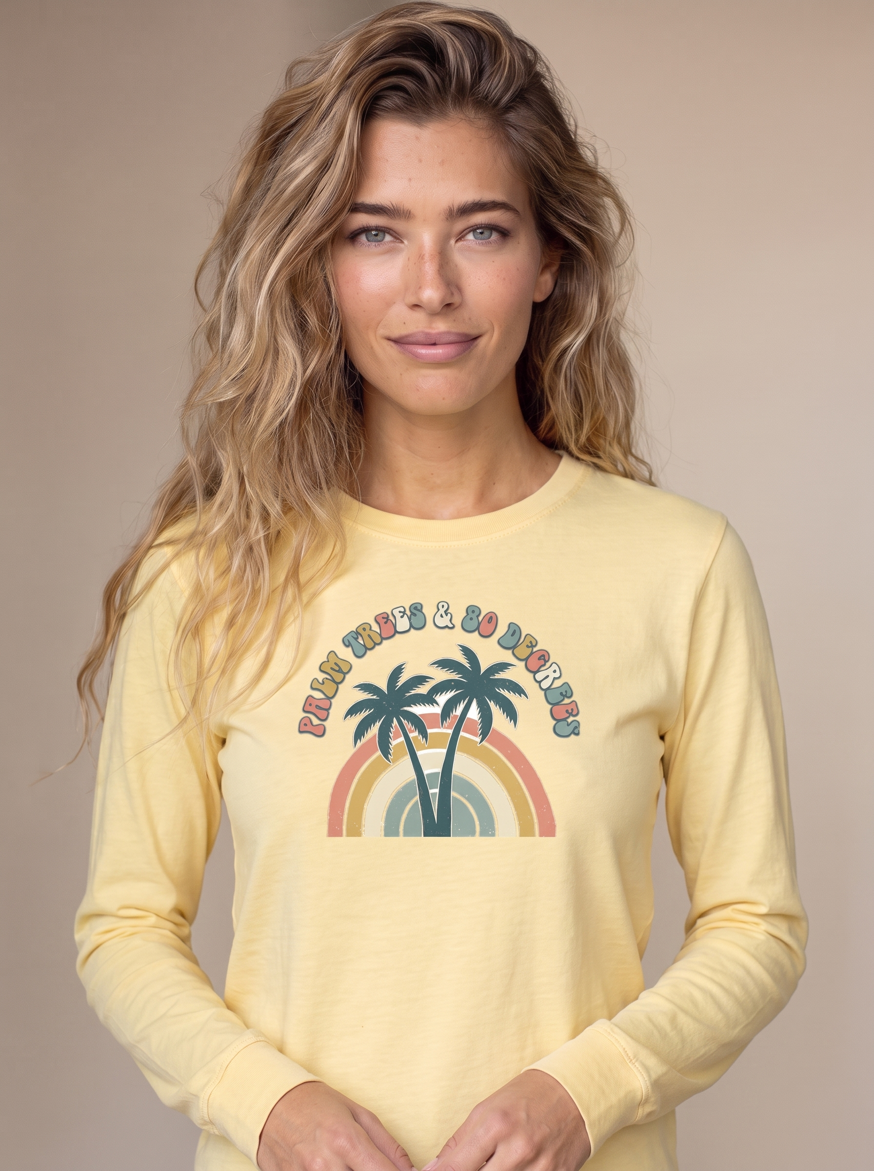 Woman wearing the Palm Trees and 80 Degrees long sleeve tee in Butter, twin palms and 70s rainbow with PALM TREES AND 80 DEGREES text centered on the chest