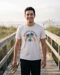 Man strolling a dune boardwalk in the Palm Trees and 80 Degrees tee in White, flip flops in hand, twin palm rainbow design on the chest