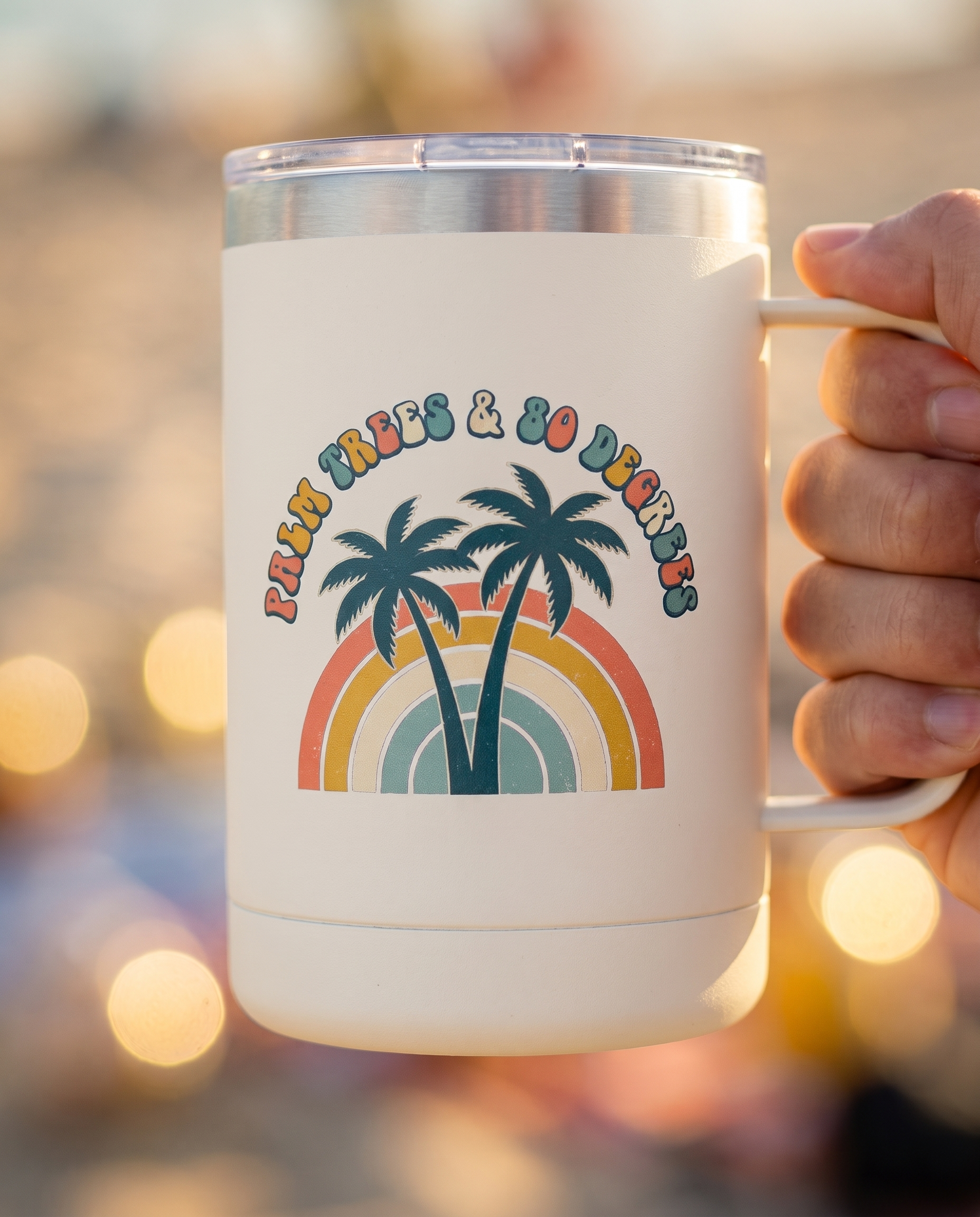 Bokeh close up of the Palm Trees and 80 Degrees 15oz tumbler, arched lettering and rainbow palms sharp against golden beach bokeh