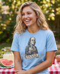 Woman laughing at a backyard July 4th picnic in the Ben Franklin TAXES tee in Carolina Blue, engraved Franklin print visible, watermelon table behind