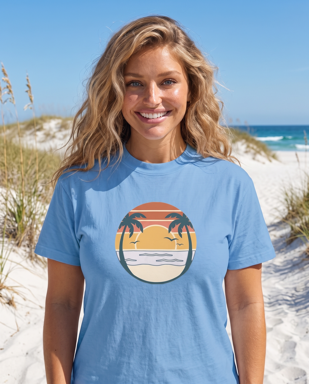 Woman on a white sand dune path with sea oats in the Retro Sunset Circle tee in Carolina Blue, striped sunset circle badge with palms at mid chest