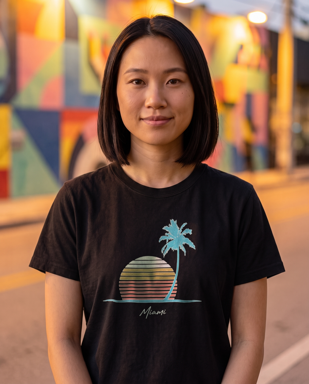 Woman on a Wynwood street at evening in the Retro Miami Palm Sunset tee in Black, single palm striped sunset print with Miami script at mid chest