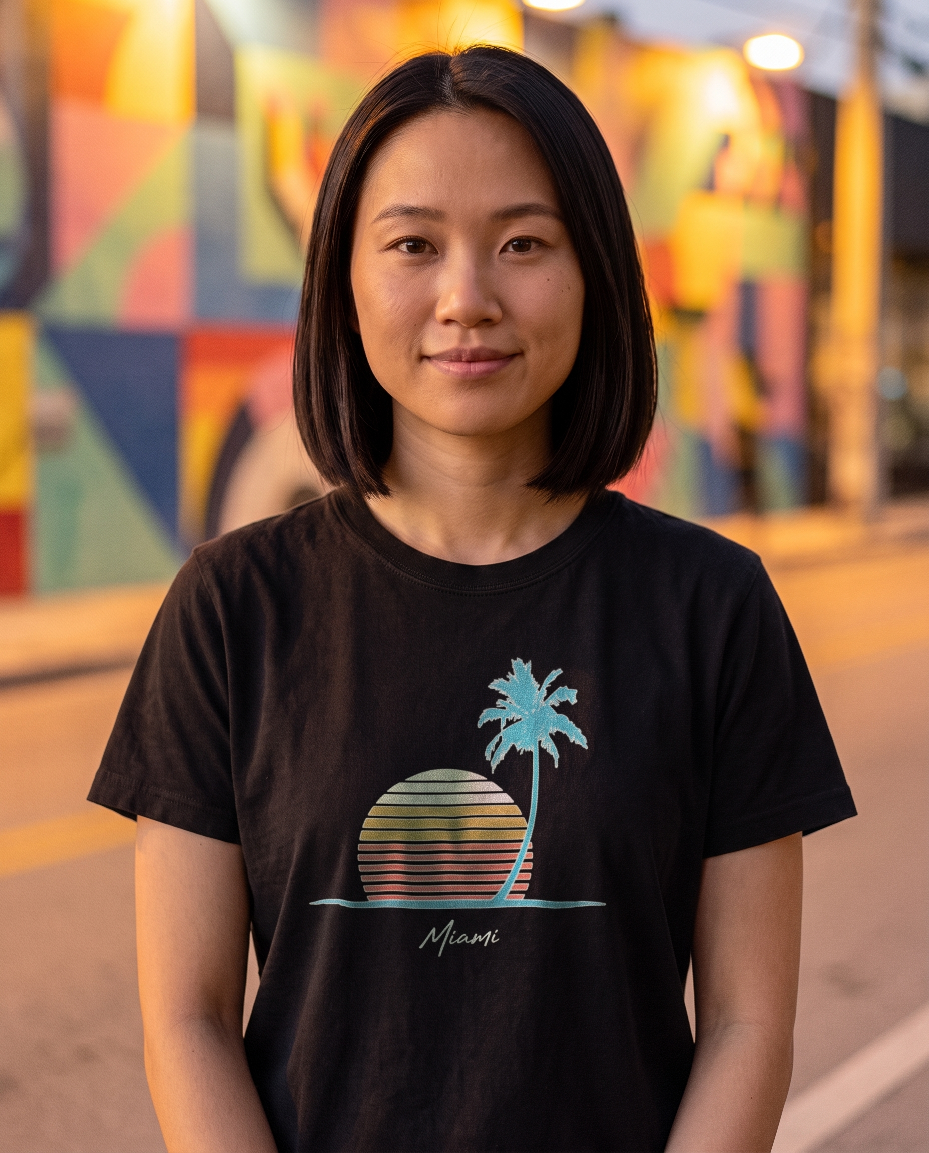 Woman on a Wynwood street at evening in the Retro Miami Palm Sunset tee in Black, single palm striped sunset print with Miami script at mid chest