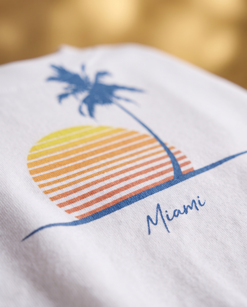 Bokeh close up of the Retro Miami Palm Sunset print on the White tee, single palm striped sunset and Miami script sharp in the cotton weave