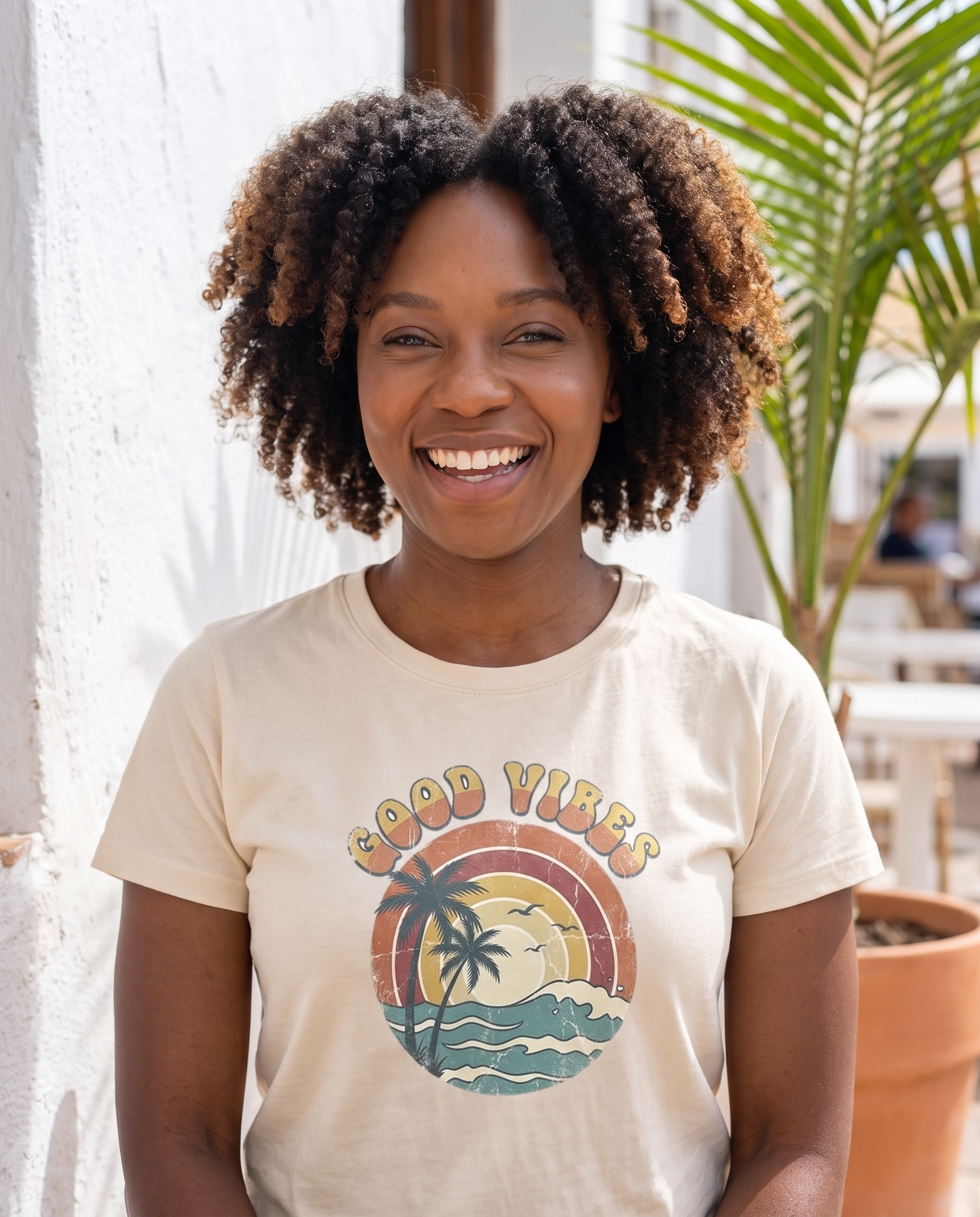 Good Vibes retro beach tee in natural cream on a coastal cafe terrace