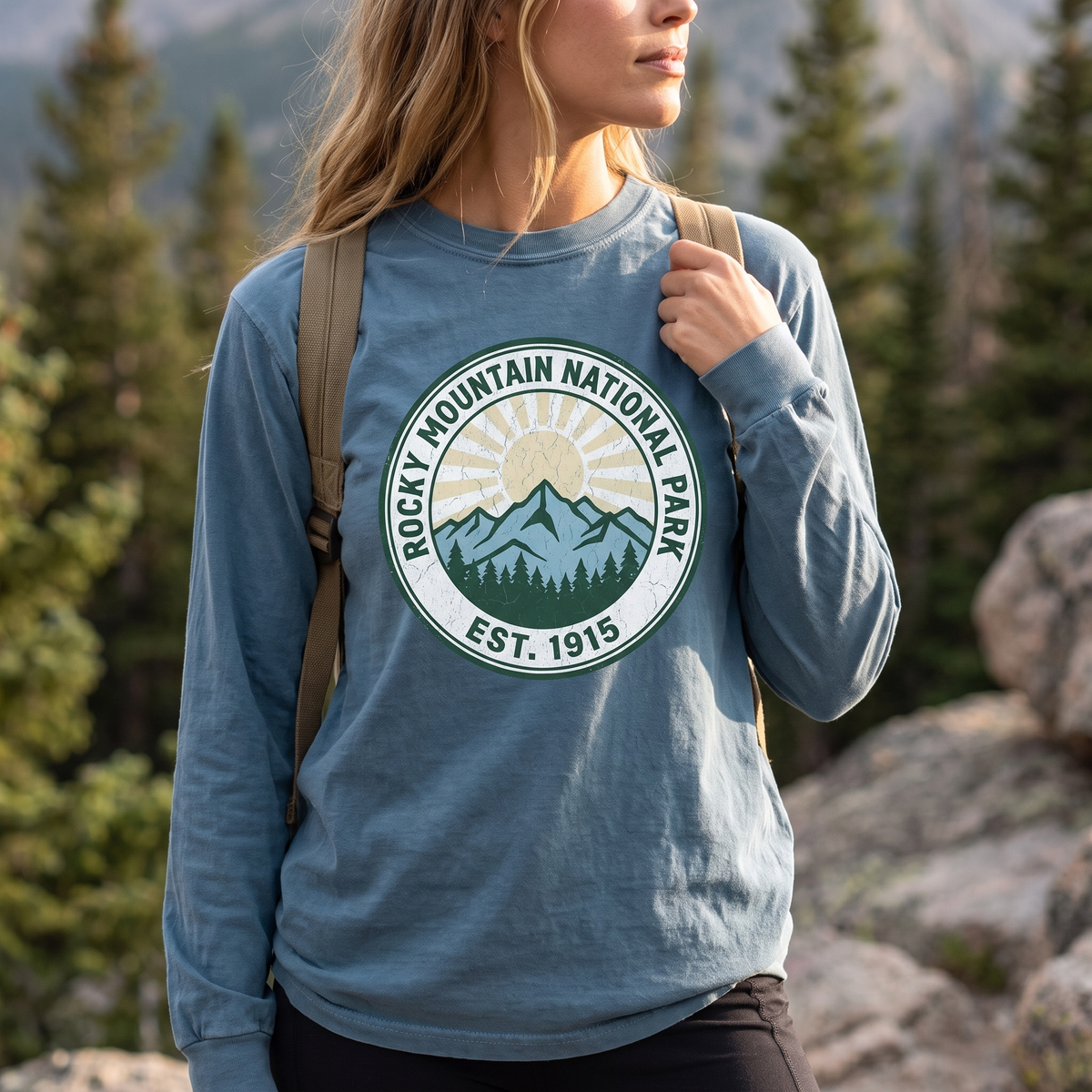 Close view of the park badge on a bay blue long sleeve tee while shouldering a daypack on the trail