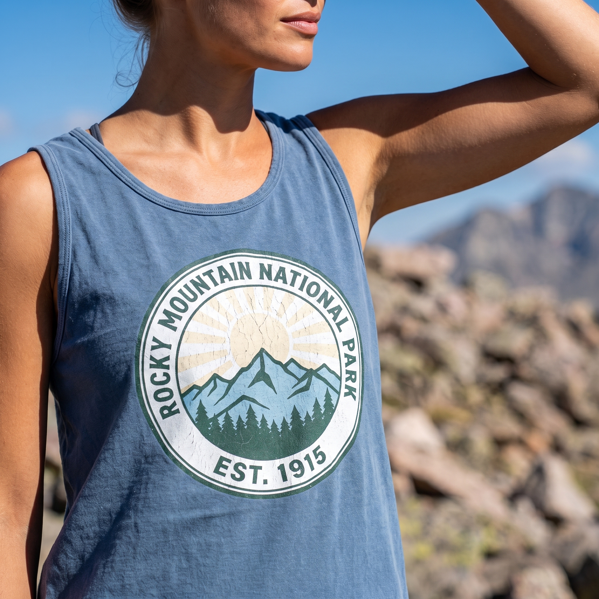 Close view of the EST. 1915 park badge on a blue jean tank top on an exposed alpine ridge in bright sun