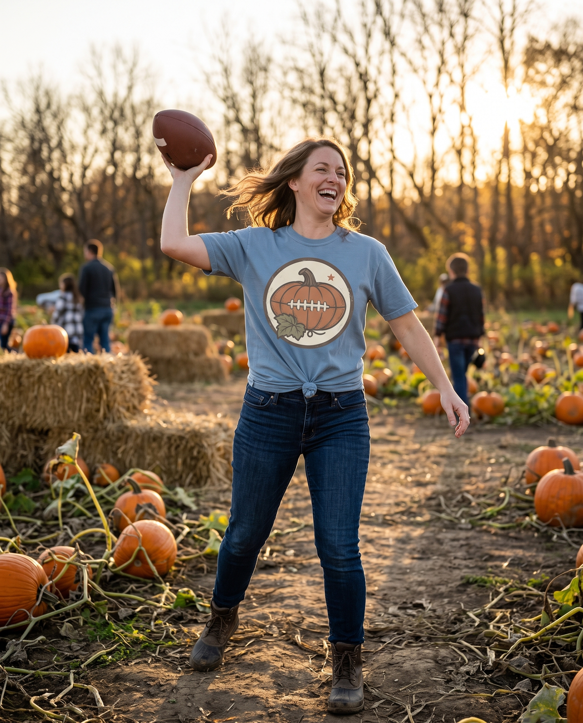 Woman in a light blue Pumpkin Football tee throwing a football across a pumpkin patch at golden hour