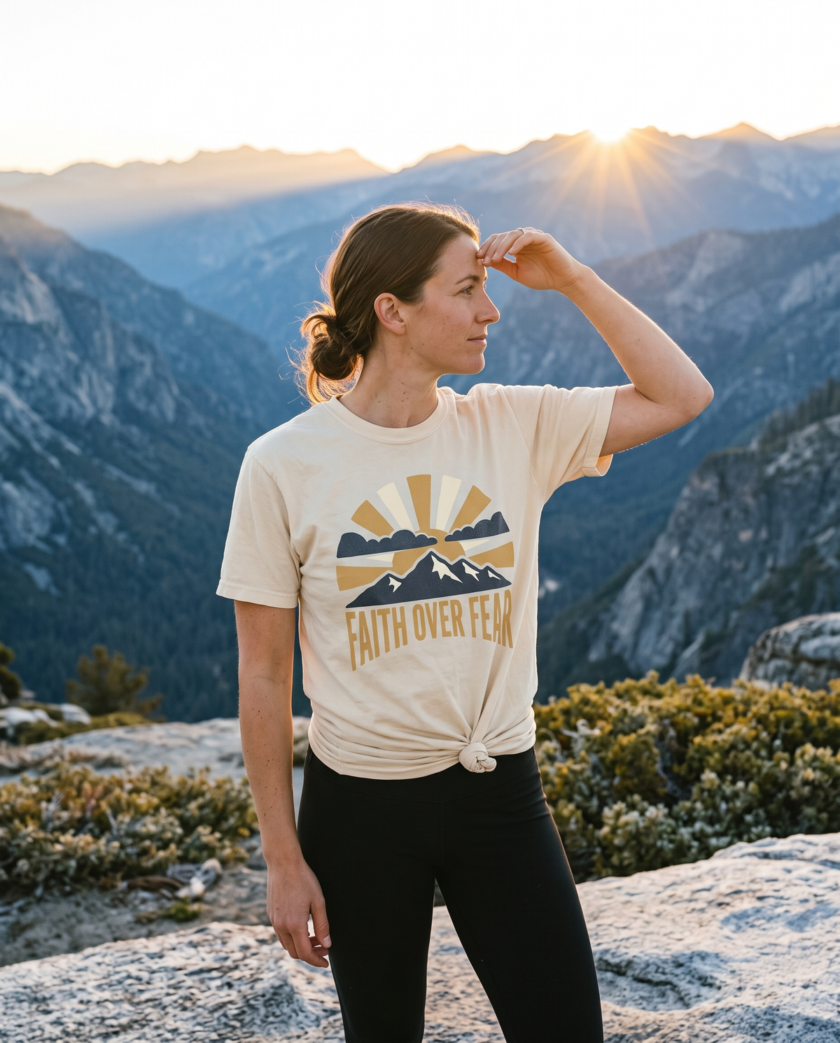 Woman in a cream Faith Over Fear tee at a mountain ridge overlook at sunrise