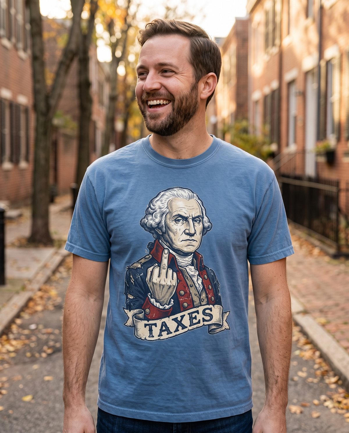 Man in a dusty blue George Washington TAXES garment-dyed tee on an old brick rowhouse street in autumn