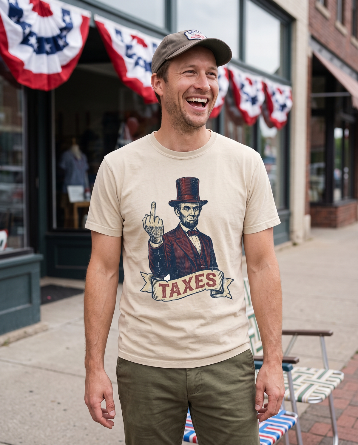 A man in a cap laughs on a main street sidewalk hung with patriotic bunting, in a cream tee printed with Abraham Lincoln and a TAXES banner.