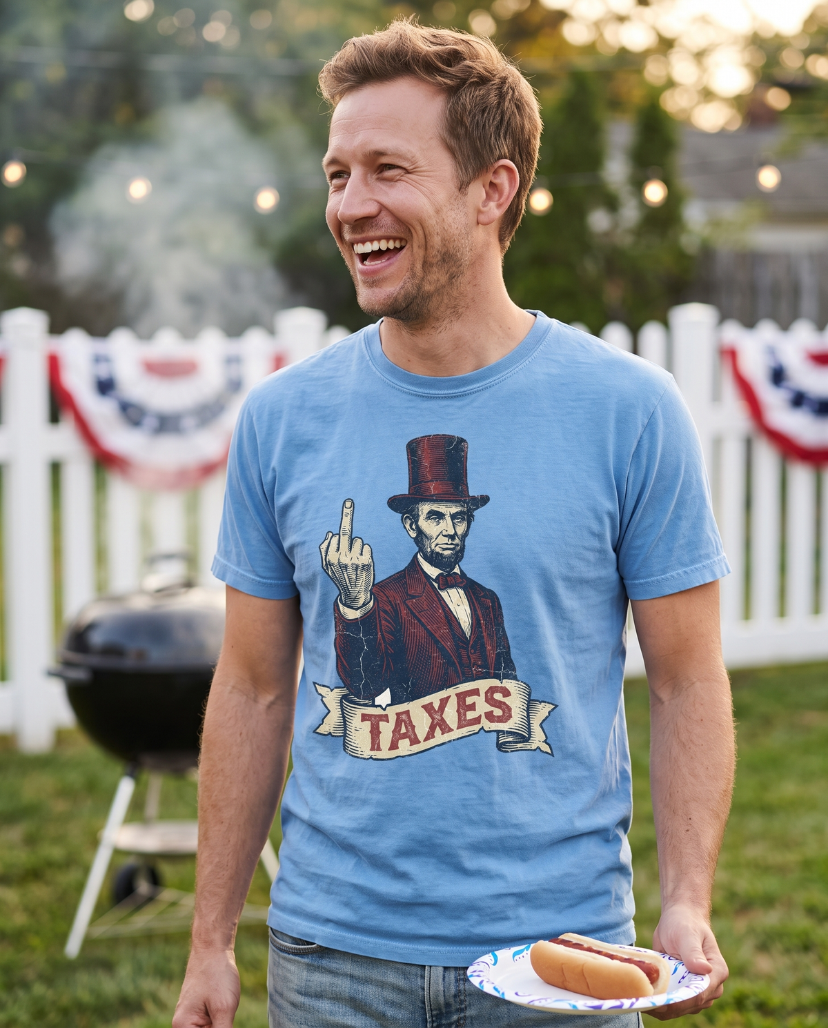 A man laughs by a charcoal grill at a bunting draped backyard party holding a hot dog plate, in a light blue tee printed with Abraham Lincoln and a TAXES banner.