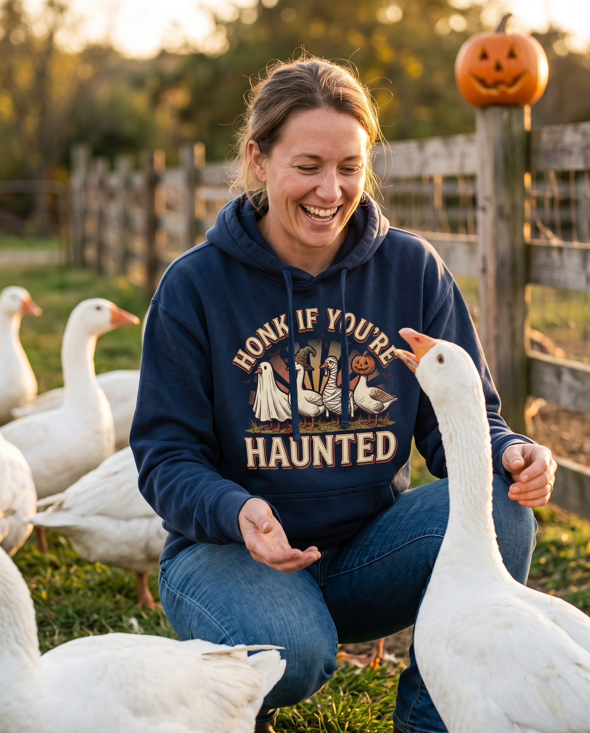 Woman in a True Navy Funny Halloween Goose hoodie crouched in a farmyard beside a flock of white geese, one hand out as a goose honks at her, laughing.