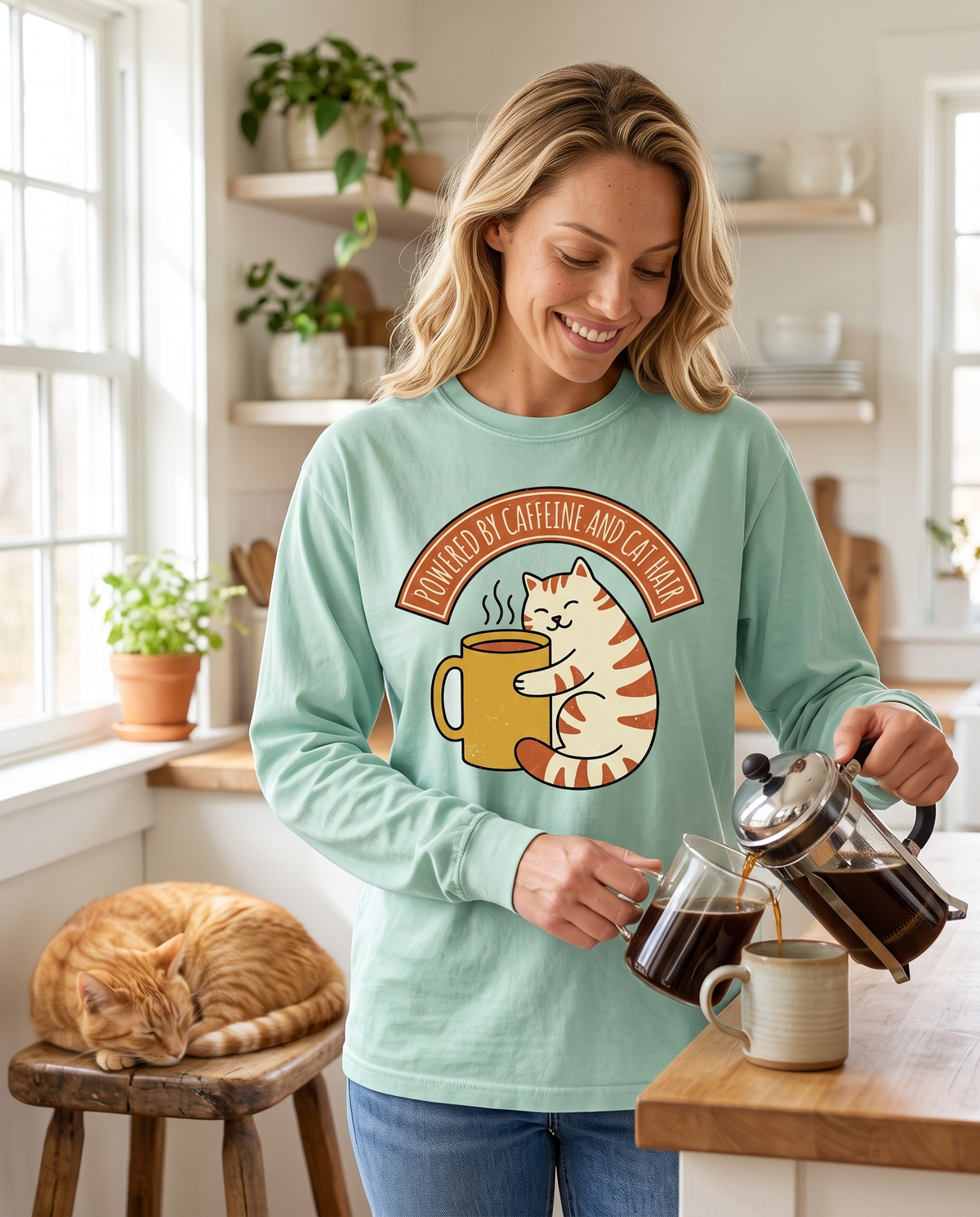 A woman pours coffee from a French press into a mug in a bright white kitchen, a ginger cat asleep on a stool beside her.