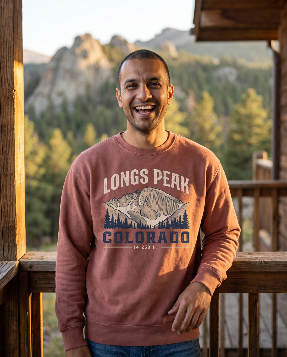 A man laughs on a cabin porch in late afternoon light, pines and a rock outcrop out of focus behind him.