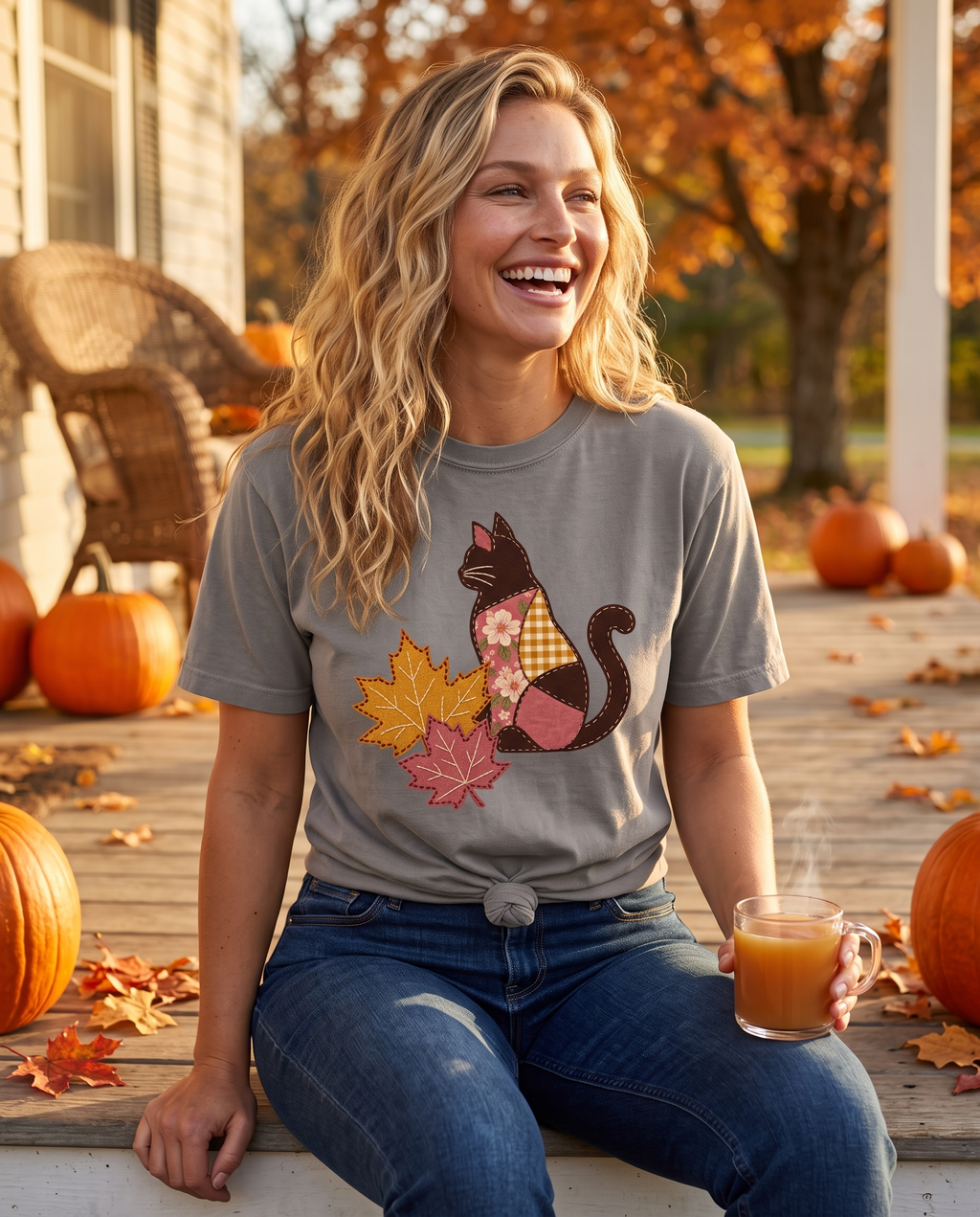 Woman laughing on a farmhouse porch among pumpkins in a Granite grey tee printed with a patchwork black cat and two fall maple leaves, lifestyle photograph