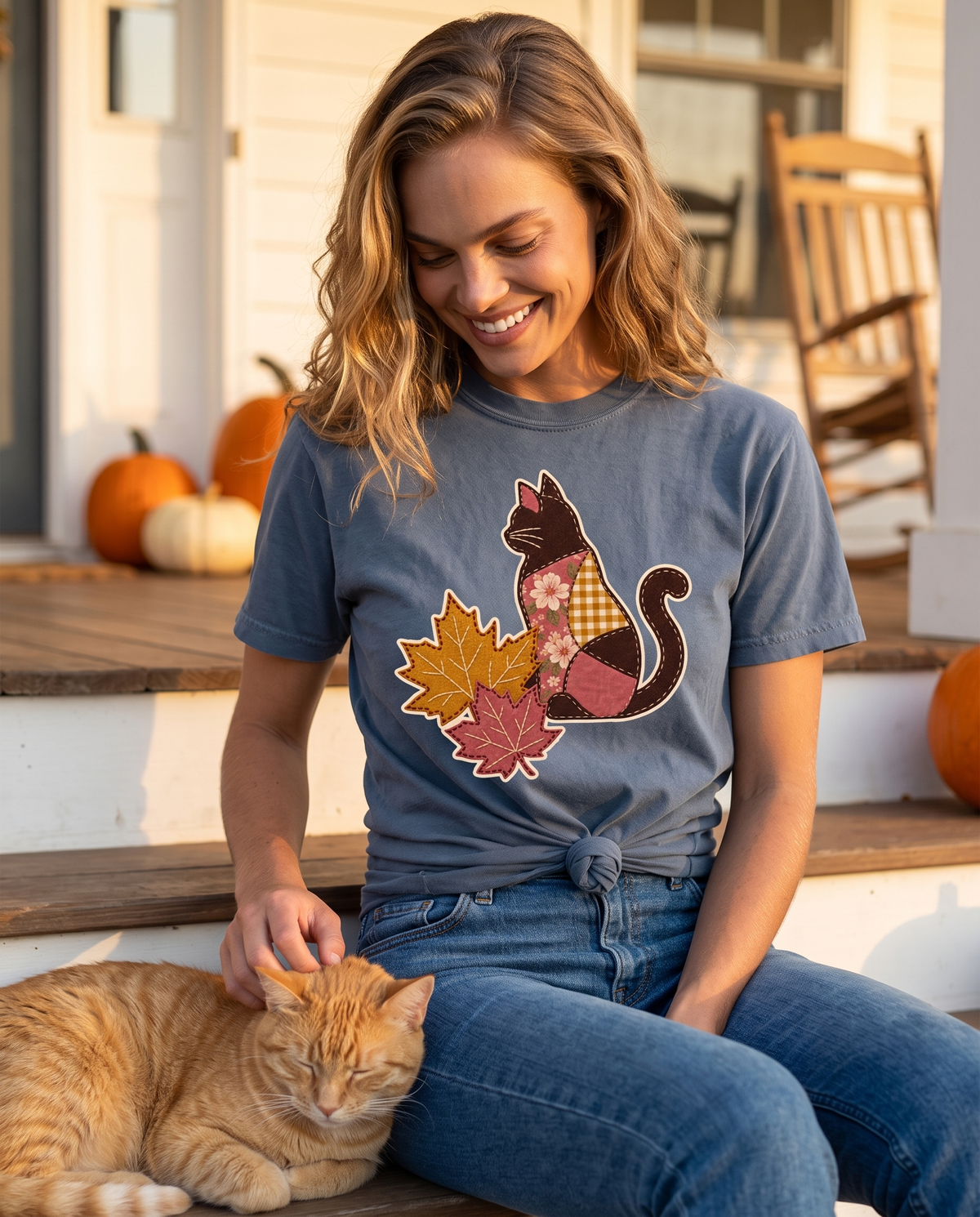 A woman sits on a white farmhouse porch step petting an orange tabby cat, with pumpkins and a wooden rocking chair behind her.
