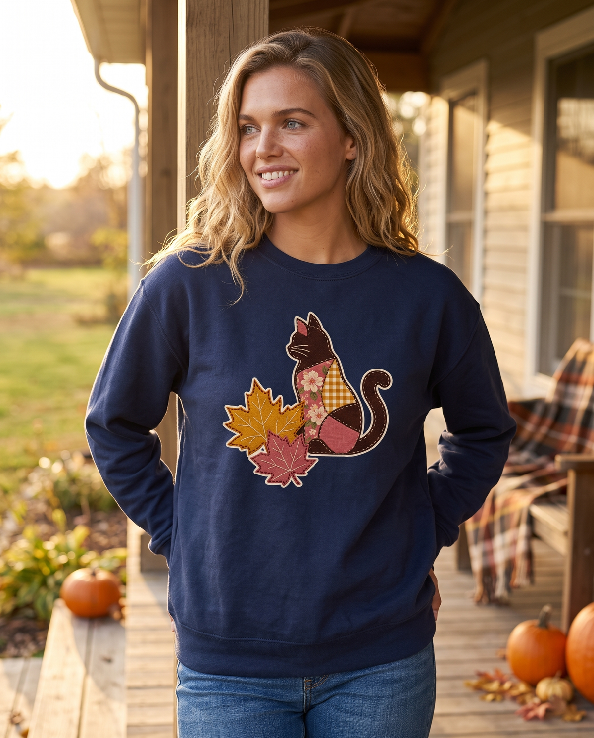 Woman on a farmhouse porch wearing a True Navy crewneck sweatshirt printed with a patchwork black cat and two fall maple leaves, lifestyle photograph