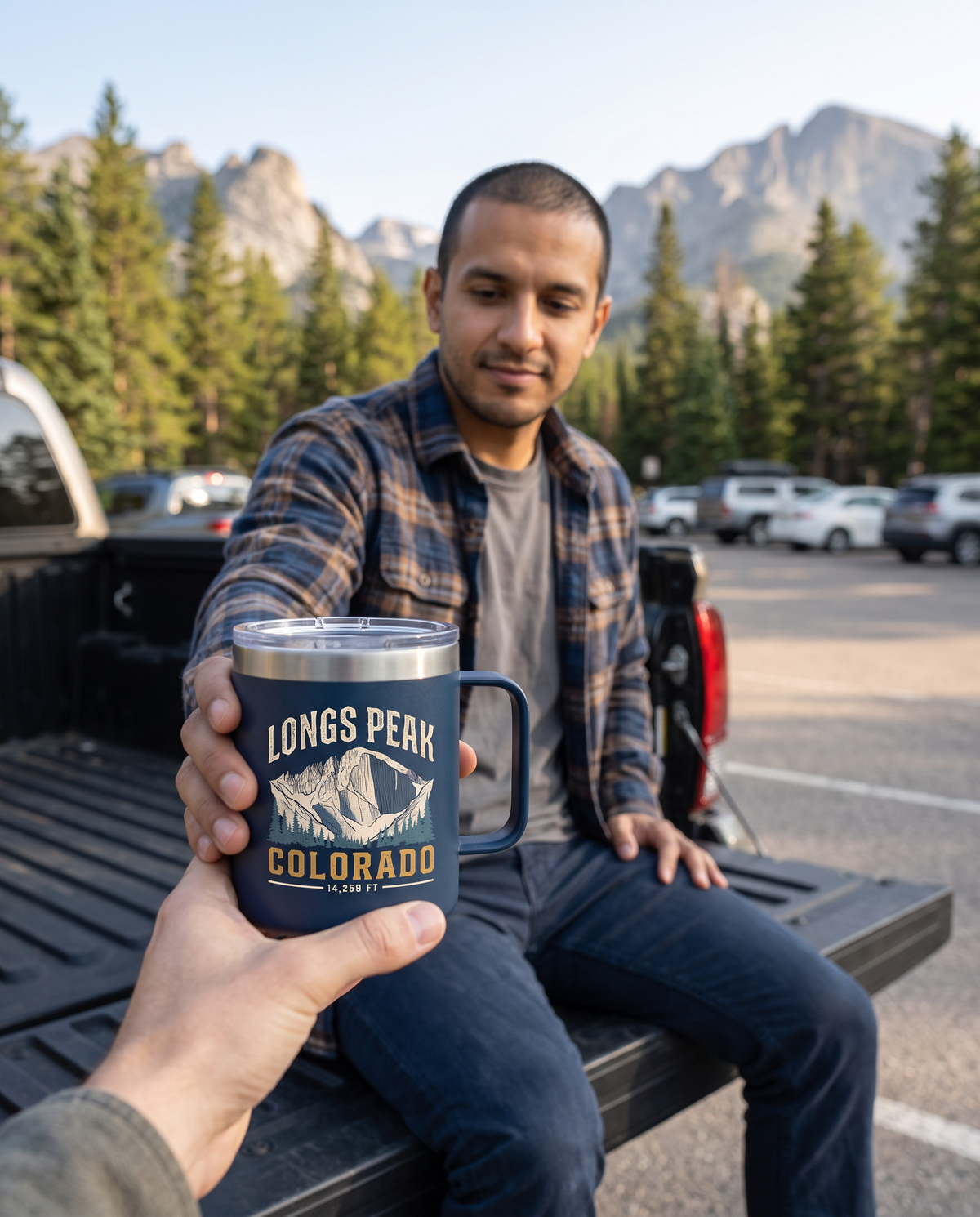 Man on a truck tailgate handing over a Navy Longs Peak Colorado 15oz coffee tumbler, 14,259 FT, lifestyle photograph