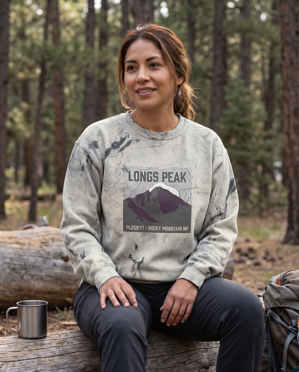 Woman at a Colorado campsite wearing the Longs Peak 14,259 ft crewneck sweatshirt in Smoke, topo summit badge design clearly visible on the chest
