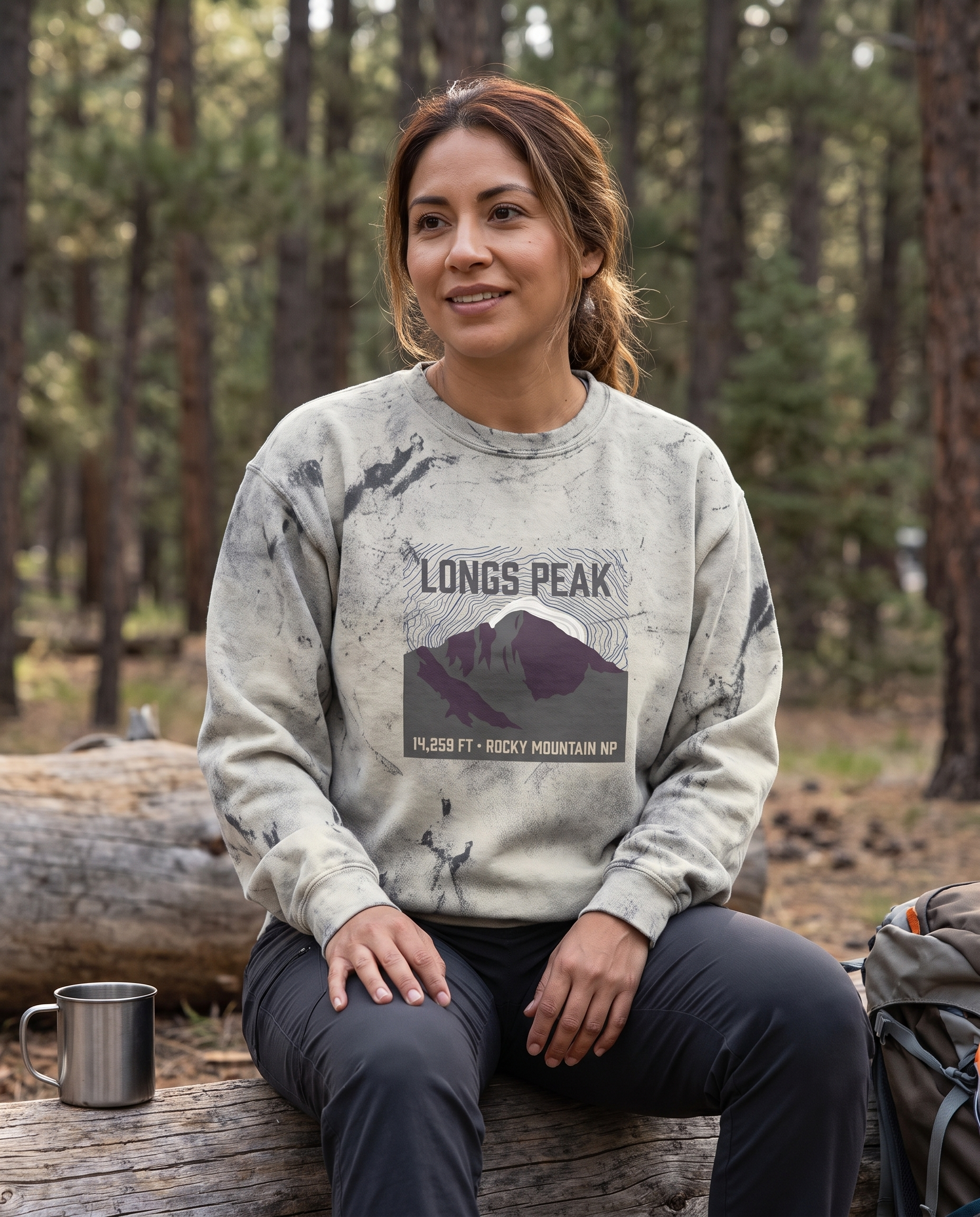 Woman at a Colorado campsite wearing the Longs Peak 14,259 ft crewneck sweatshirt in Smoke, topo summit badge design clearly visible on the chest