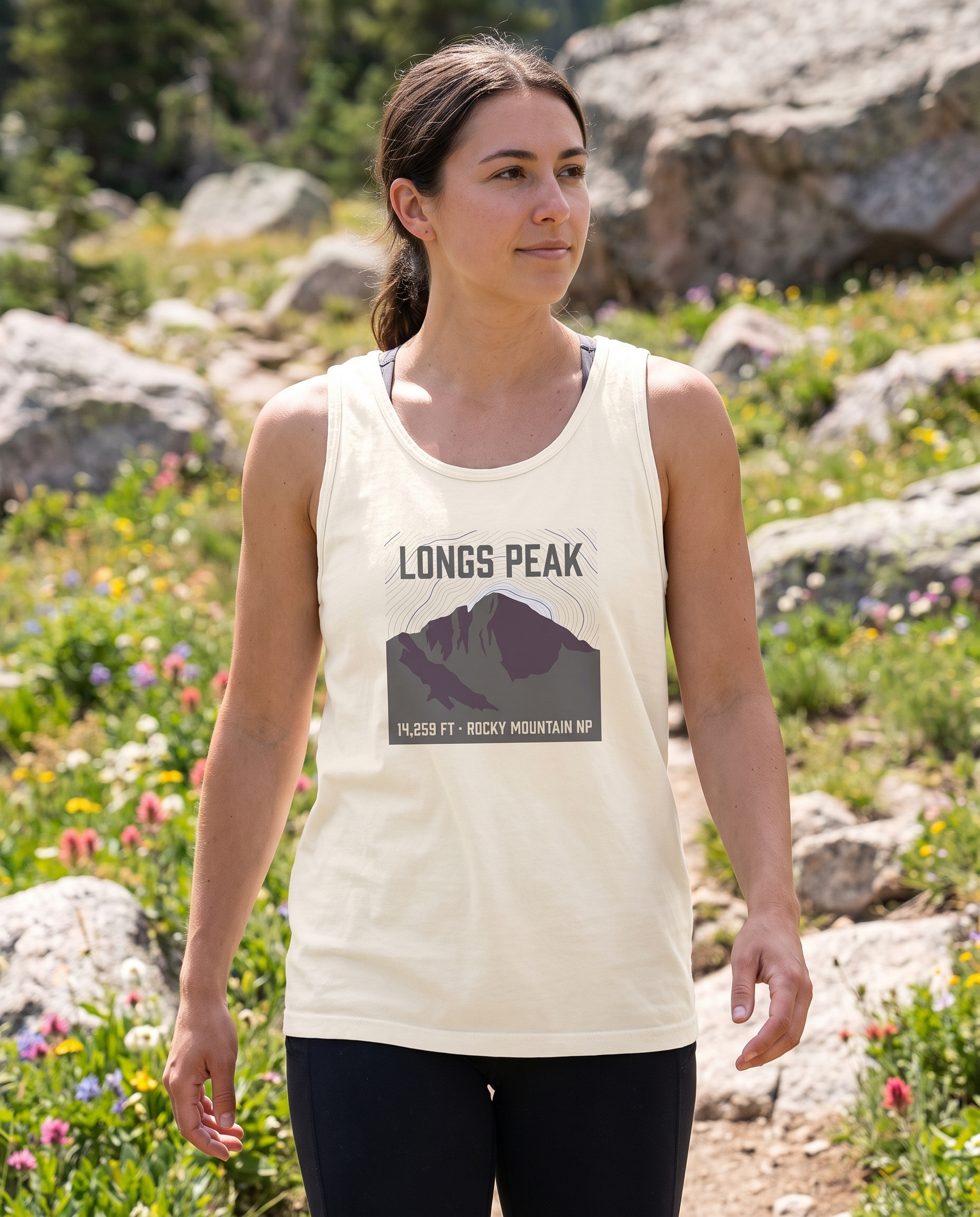 Woman hiking an alpine wildflower trail in the Longs Peak 14,259 ft tank top in Ivory, topo summit badge design clearly visible on the chest