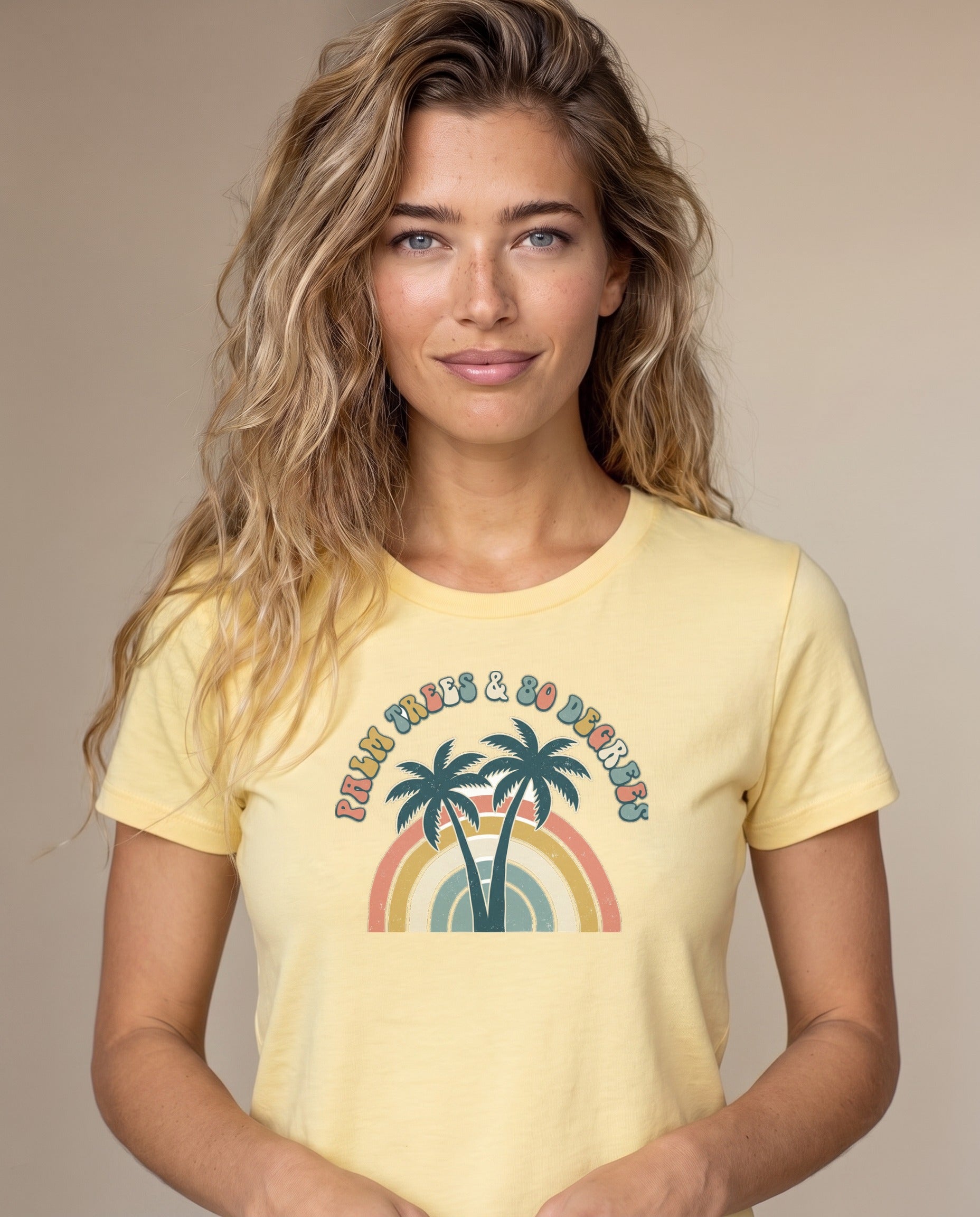 Woman wearing the Palm Trees and 80 Degrees retro rainbow summer tee in Butter, Comfort Colors garment-dyed cotton, twin palms and 70s rainbow arch design, waist-up natural light portrait