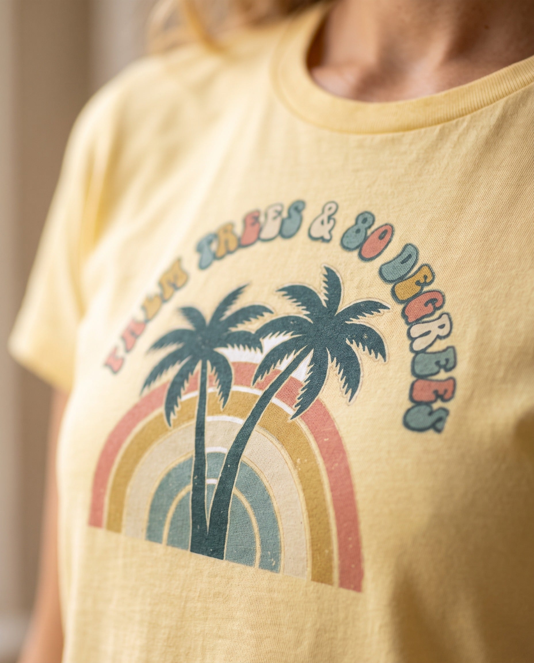 Close-up detail of the Palm Trees and 80 Degrees screen print on a Butter garment-dyed Comfort Colors tee, showing soft cotton texture and vintage matte ink, shallow depth of field