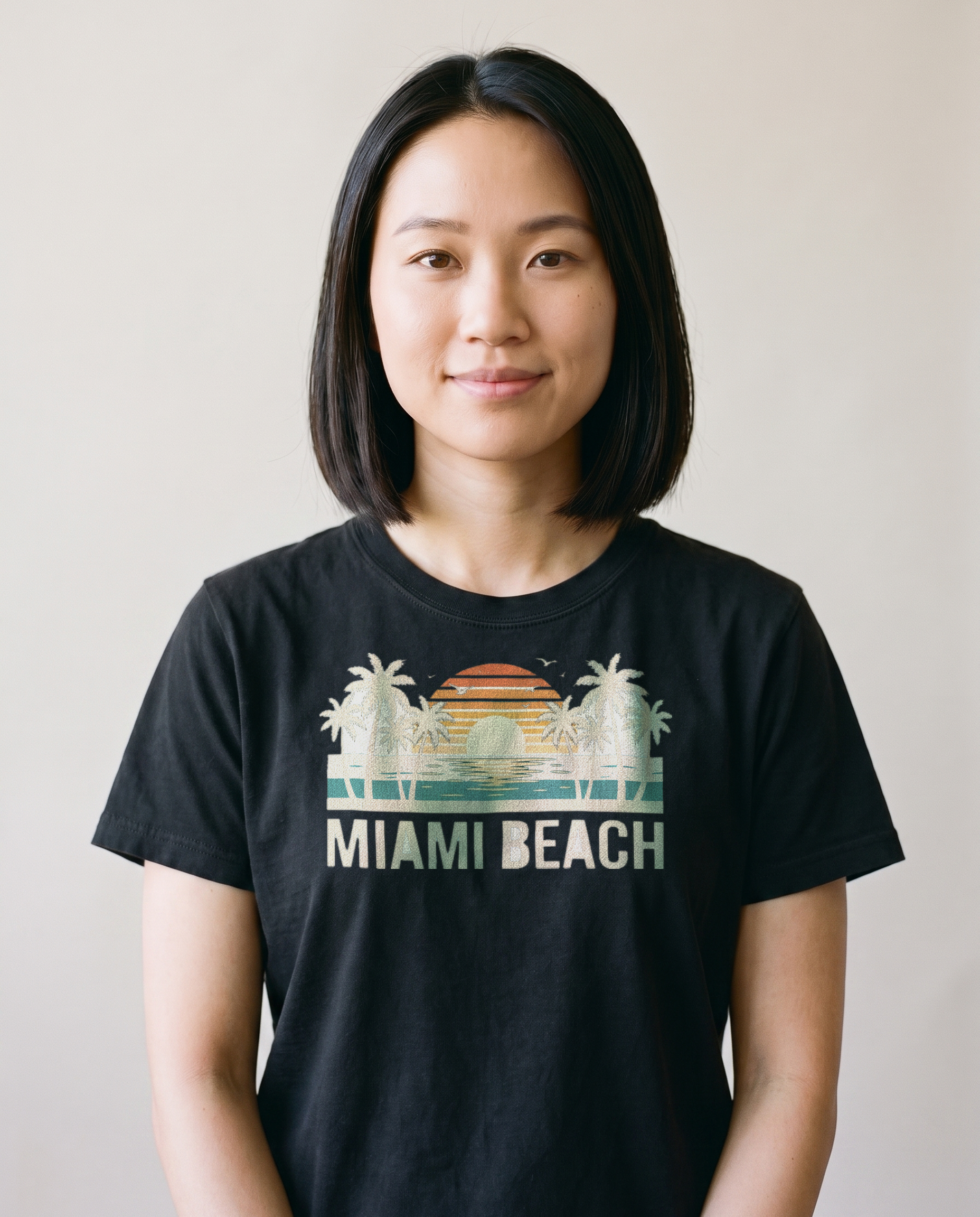 Woman wearing the Miami Beach retro tee in Black, cream palms and sunset with MIAMI BEACH lettering centered on the chest